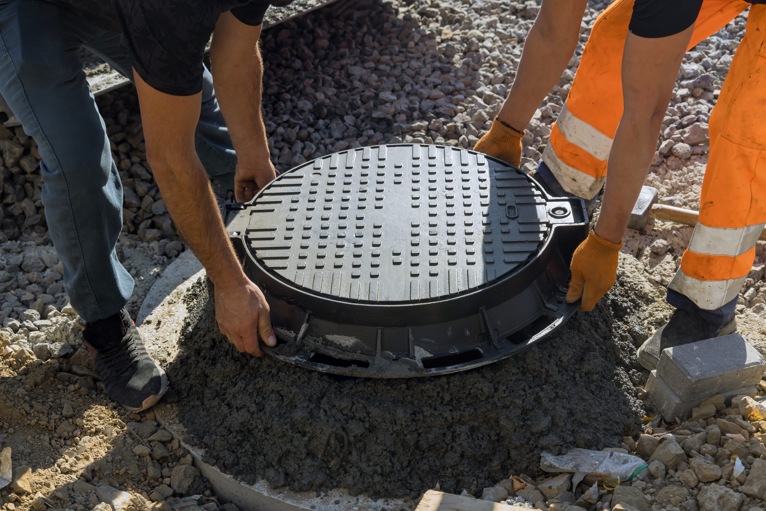 A worker installs a sewer manhole on a septic tank made of concrete rings on Simphome